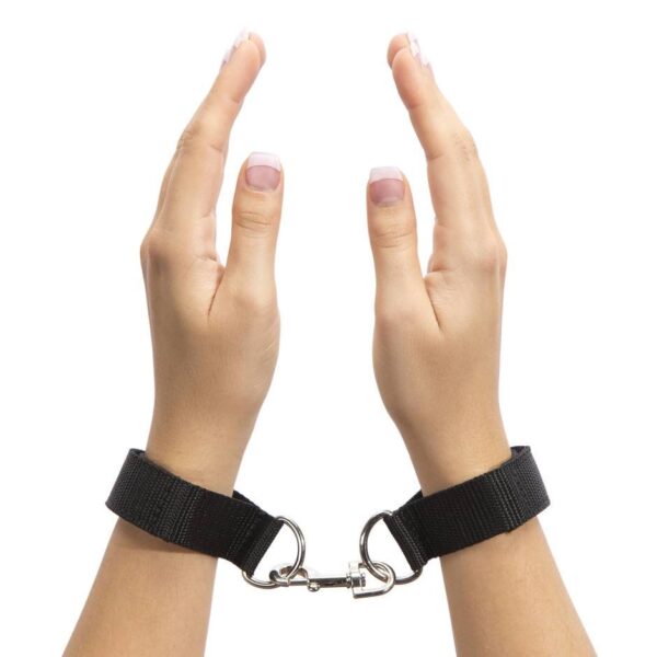 "Adjustable black wrist restraints with a metal connector clip, shown on hands with manicured nails."