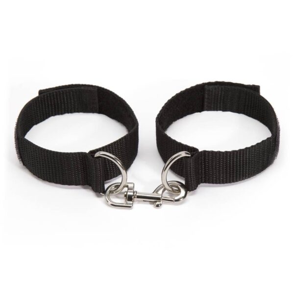 "Adjustable black wrist restraints with a metal connector clip, shown on hands with manicured nails."