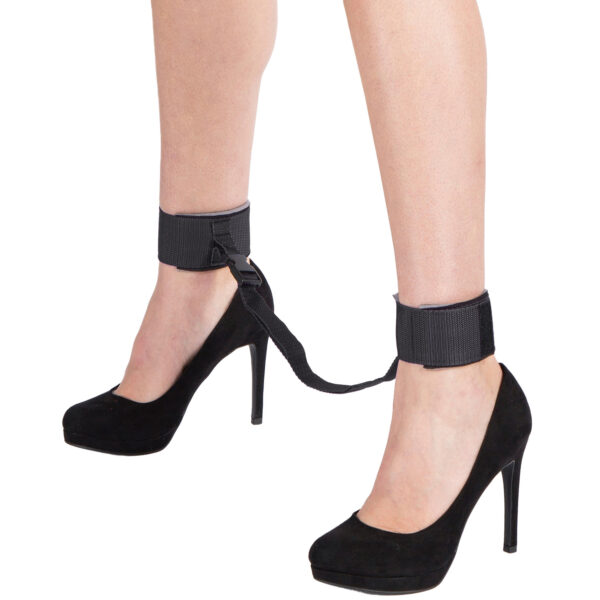 Close-up of black ankle cuffs with adjustable straps, connected by a durable black strap, worn by a model in high heels.